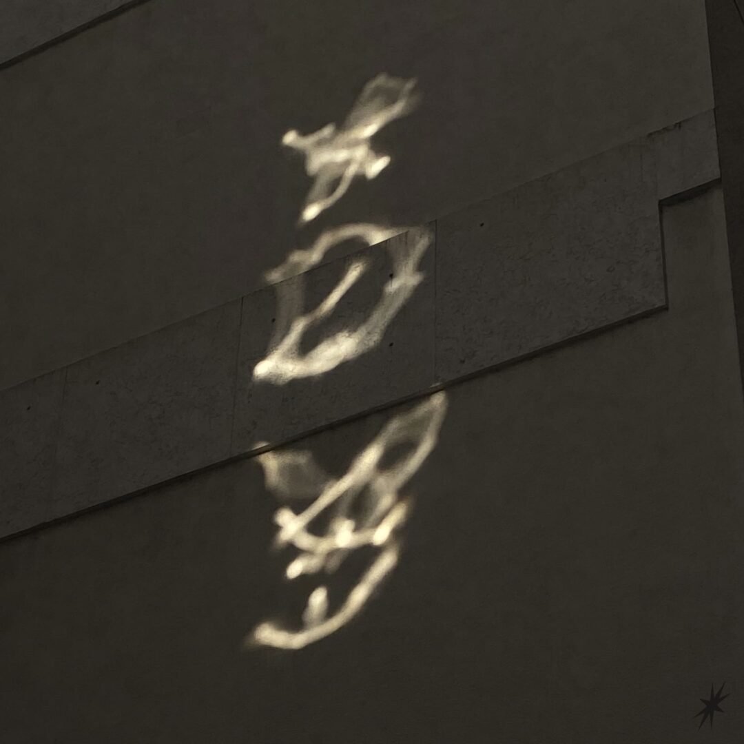 Light forms XDY patterns on a textured gray wall, creating a mysterious and serene atmosphere with soft highlights and shadows.