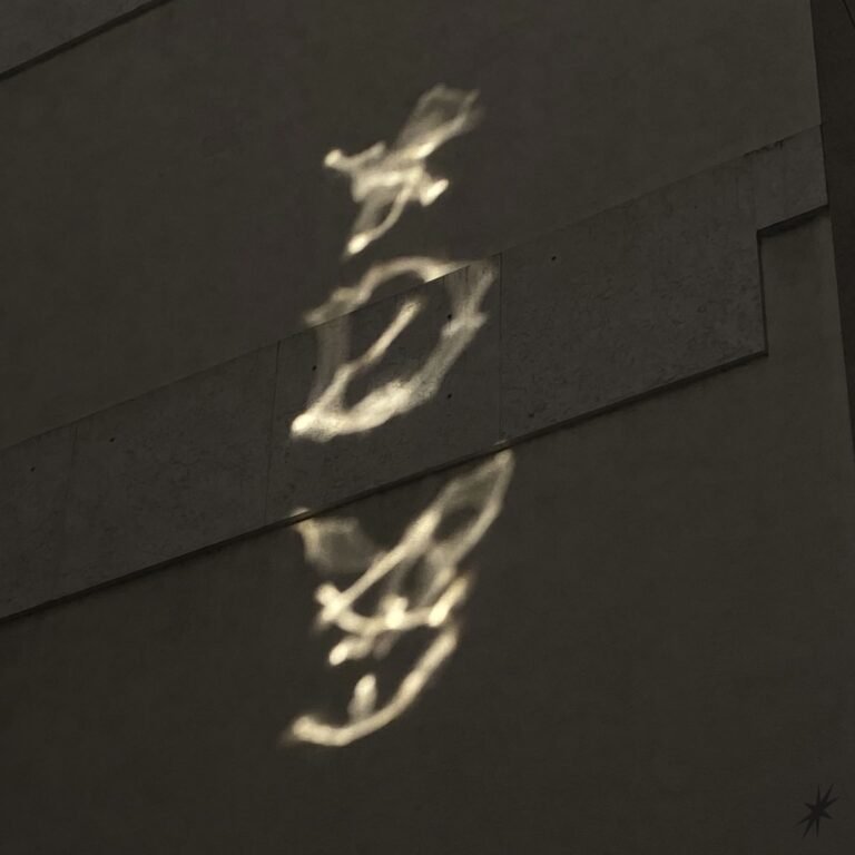 Light forms XDY patterns on a textured gray wall, creating a mysterious and serene atmosphere with soft highlights and shadows.